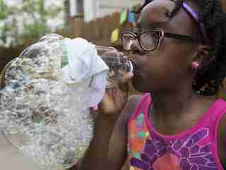 A young girl uses a plastic bottle to blow bubbles