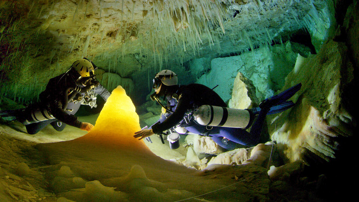 Divers look at a formation in an underwater cave