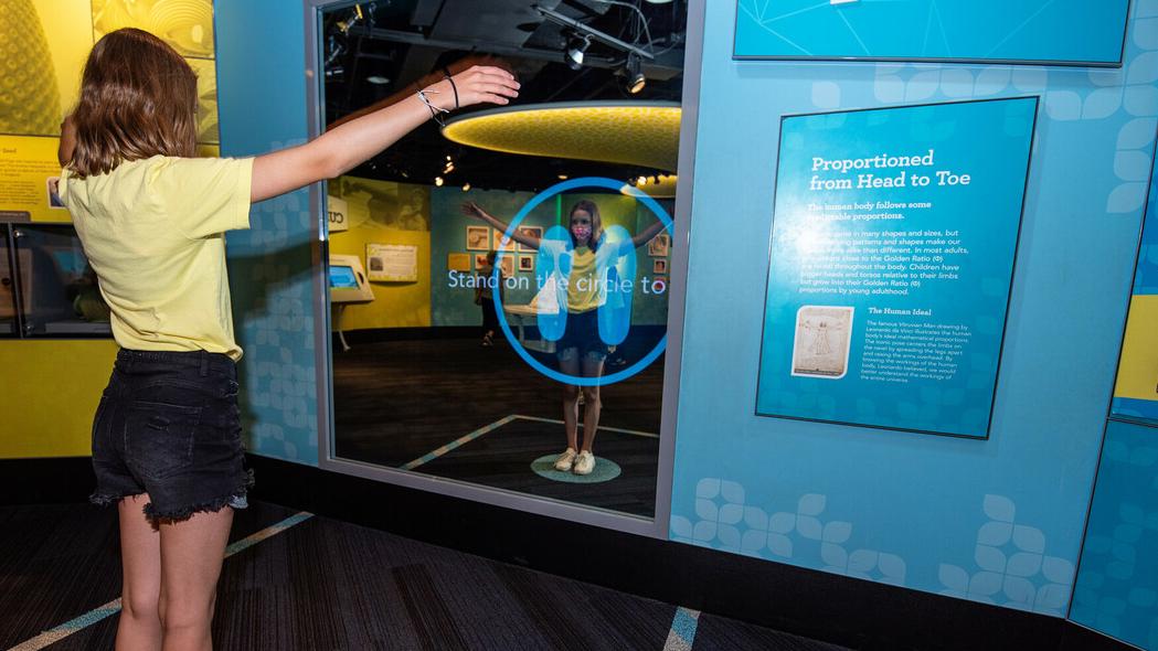 Image of a girl standing with arms outstretched before a mirrored interactive.