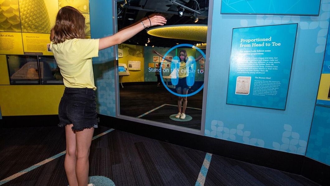 Image of a girl standing with arms outstretched before a mirrored interactive.